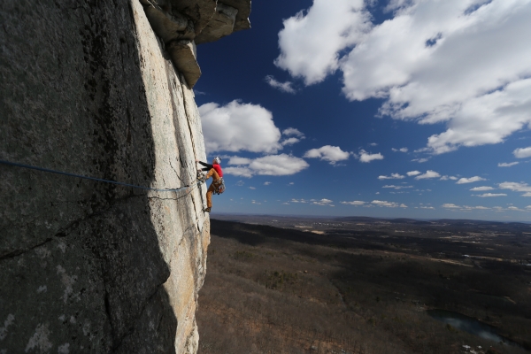 A climber high on a Gunks route, with the valley spread out below.